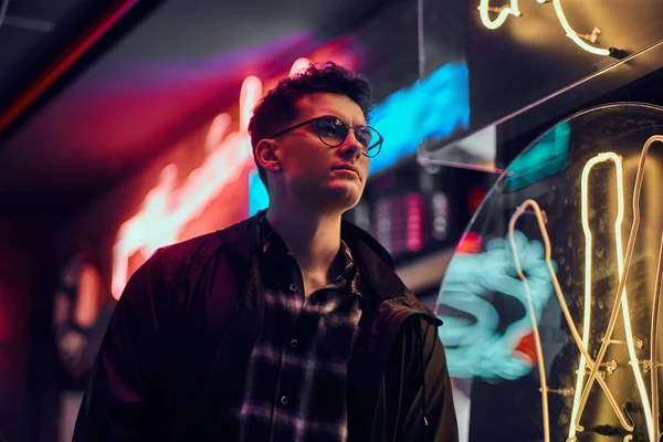 Un joven guapo de pie por la noche en la calle. Letreros iluminados, neón, luces . — Foto de Stock