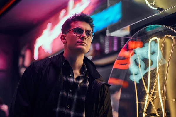 Een knappe jongeman permanent 's nachts in de straat. Verlichte borden, neon, verlichting. — Stockfoto