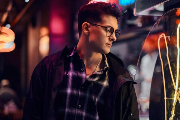 Geceleri sokakta ışıklı tabela bakarak dalgın bir genç adam.