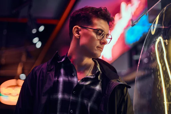 Geceleri sokağa ışıklı tabela bakarak spor kapüşonlu genç dalgın bir adam portresi.