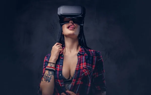 Menina tatuada vestindo uma camisa desabotoada vermelha verificada usando um fone de ouvido VR . — Fotografia de Stock