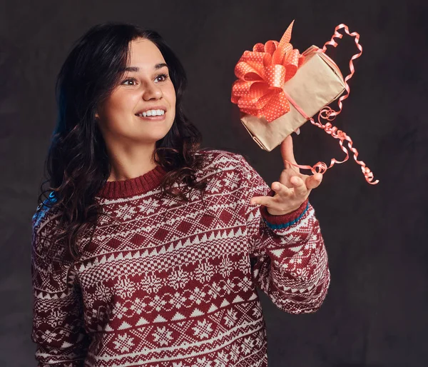 Портрет щасливої дівчини брюнетки в теплому светрі дівчина викидає подарункову коробку, ізольовану на темному текстурованому фоні . — стокове фото