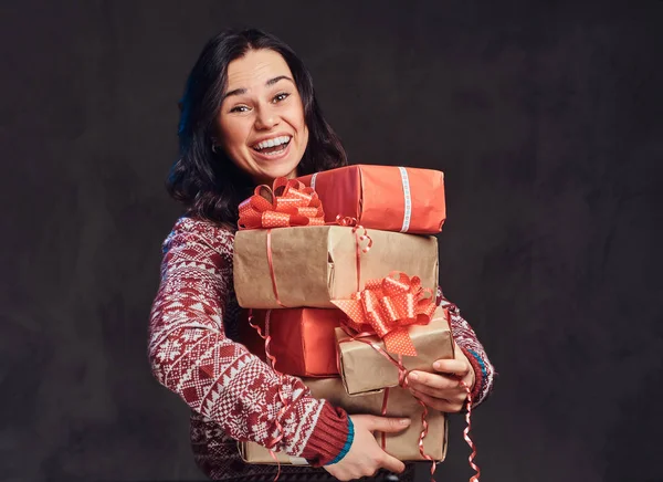 Portret van een gelukkig brunette meisje draagt een warme trui houden een geschenken-dozen, geïsoleerd op een donkere gestructureerde achtergrond. — Stockfoto