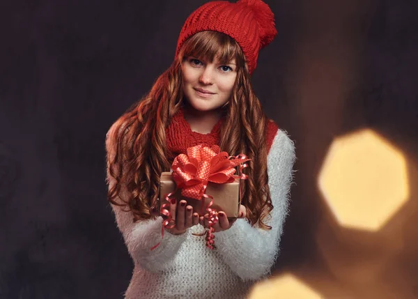 Retrato de uma linda menina ruiva sorridente vestindo uma camisola quente e cachecol segurando uma caixa de presente . — Fotografia de Stock