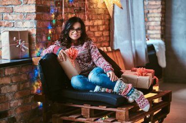 Çatı katı iç ile dekore edilmiş bir odada hediye kutuları ile bir kanepede oturan neşeli güzel kız.