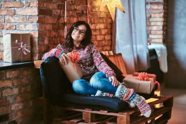 Yılbaşı, Sevgililer günü, yeni yıl. Çatı katı iç ile dekore edilmiş bir odada hediye kutuları ile bir kanepede oturan neşeli güzel kız.