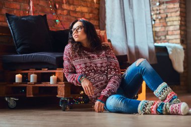 Beautiful girl sitting on a floor and looking out the window in a decorated room with loft interior.
