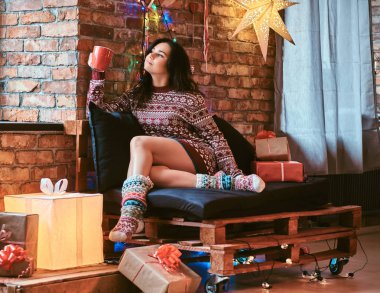 Güzel kız bir fincan kahve ile ısınma çatı iç ile dekore edilmiş bir odada bir kanepede otururken Noel sabahı zevk.