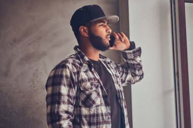 Afrikalı-Amerikalı bir kareli gömlek ve telefonla konuşurken kap giyen adam sakallı