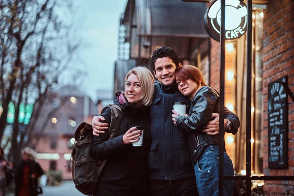 Happy friends standing together in an embrace near a cafe outside. — Stock Photo, Image