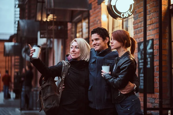 Веселые друзья, стоящие вместе в объятиях возле кафе снаружи, смотрят в сторону . — стоковое фото