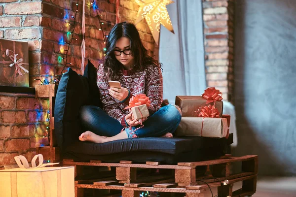 Beautiful girl chatting with friends while sitting on a couch with gift boxes in a decorated room with loft interior. — Stock Photo, Image