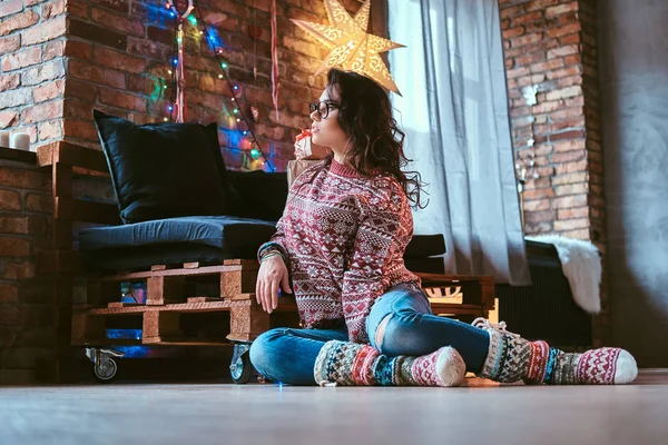 Beautiful girl sitting on a floor and looking out the window in a decorated room with loft interior. — Stock Photo, Image