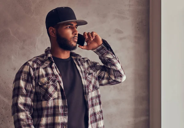 Africano-americano barbudo homem vestindo uma camisa xadrez e boné falando por telefone — Fotografia de Stock