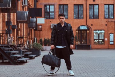 Poz ve kameraya sokakta arayan genç adam trendy giymiş.