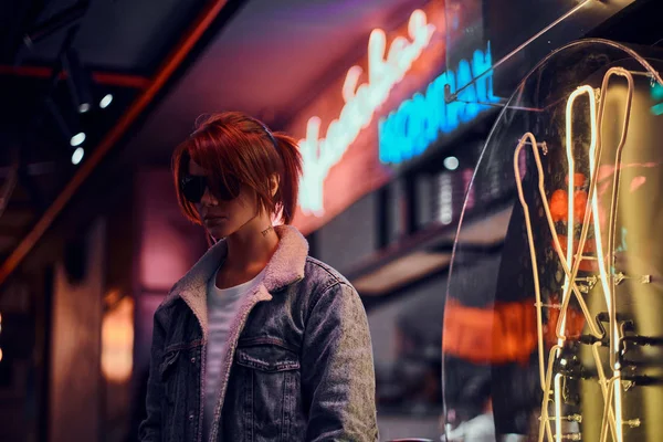 Stylový zrzka dívka stojící v noci na ulici. Obchod štíty, neon, světla. — Stock fotografie