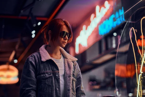Menina ruiva elegante de pé na noite na rua. Sinais de loja, néon, luzes . — Fotografia de Stock
