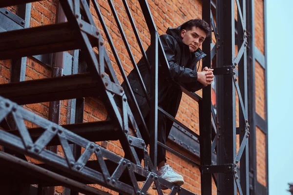 Een modieuze man leunend op een leuning trap buiten het gebouw met de industriële buitenkant. — Stockfoto