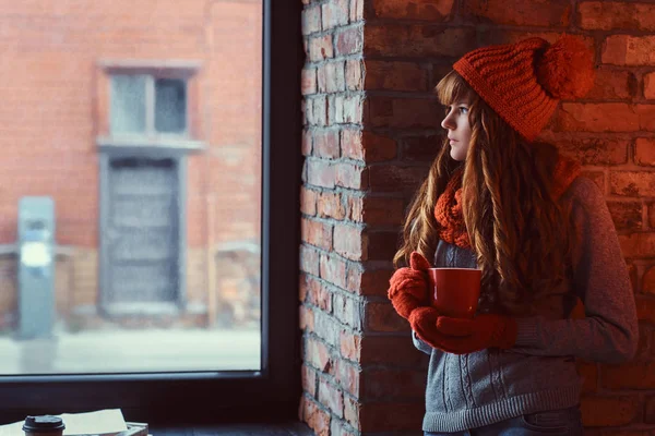 圣诞节 情人节 一个孤独的红头发的女孩穿着一件暖和的毛衣 戴着一杯咖啡 一边靠在砖墙上 望着窗外 她的肖像 — 图库照片