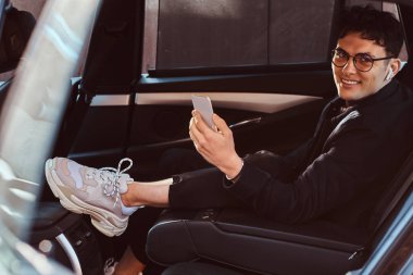 Yakışıklı bir genç adam bir smartphone lüks arabanın arka koltuğunda dinlenirken holding.