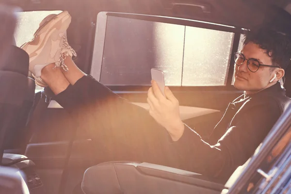 stock image A handsome young man using a smartphone while relaxing in the back seat of the luxury car.