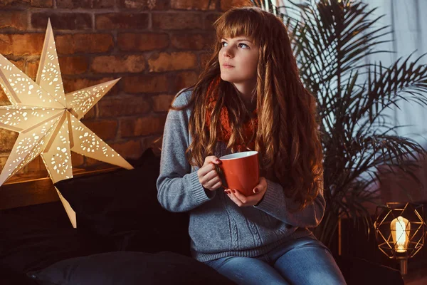 Redhead girl warming with a cup of coffee in a decorated living room at Christmas time. — Stock Photo, Image