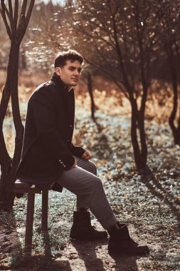 Sonbahar ormandaki bir bankta oturmuş siyah bir ceket giyen genç bir adam