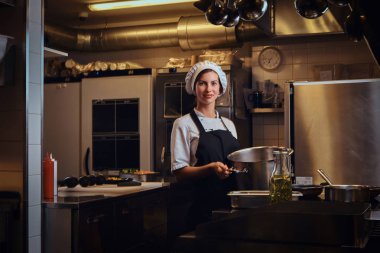 Kadın şef bir pan tutan bir üniforma giyen bir kamera bir mutfak bir bakarak gülen.