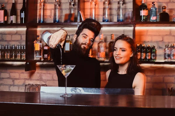 Un barman barbu au regard confiant fait un cocktail avec une belle fille derrière le comptoir du bar — Photo