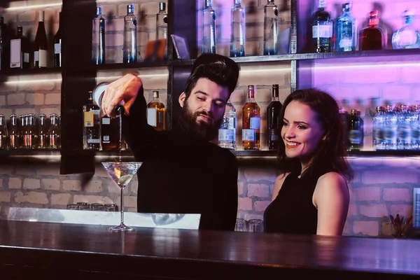 Un barbuto barista con un aspetto fiducioso fa un cocktail con una bella ragazza dietro il bancone del bar — Foto Stock