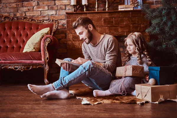 Love, family, fatherhood, Christmastime. Handsome father reads his daughter fairy tales while they sitting on the floor surrounded by gifts — Stock Photo, Image