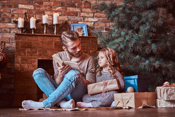 Love, family, fatherhood, Christmastime. Handsome father reads his daughter fairy tales while they sitting on the floor surrounded by gifts — Stock Photo, Image
