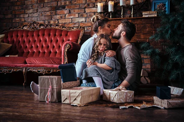 Felicidade bonito menina sentada com seus pais em um chão cercado por presentes, ao lado da lareira e árvore de natal — Fotografia de Stock