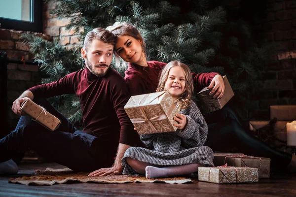 有吸引力的家庭坐在圣诞树旁边的地板上打开礼物. — 图库照片