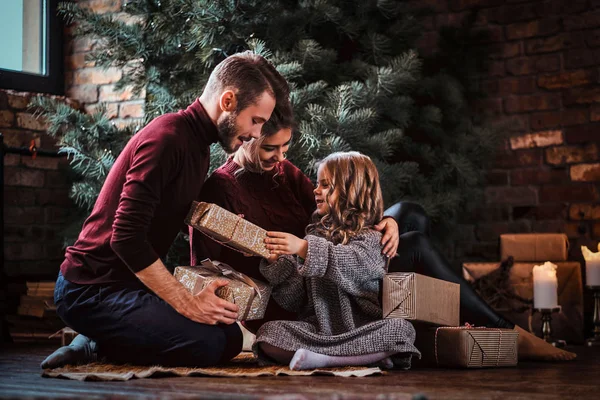 Attractive family opens presents while sitting on a floor next to the Christmas tree. — Stock Photo, Image