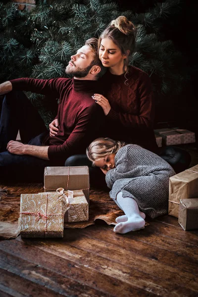 Attractive family relaxing while sitting together on a floor surrounded by gifts next to the Christmas tree. — Stock Photo, Image