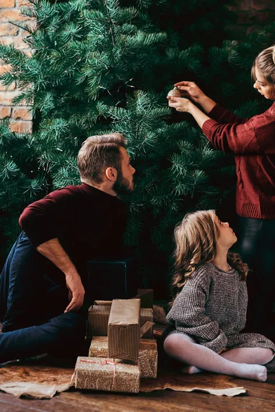 Attractive family decorates the Christmas tree, surrounded by gifts at home. — Stock Photo, Image