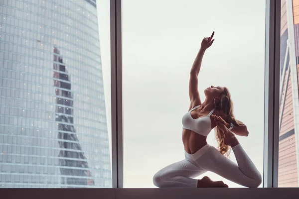 Krásná dívka, která nosí sportovní oblečení děláte cvičení jógy na okenním parapetu v bytě mrakodrap. — Stock fotografie