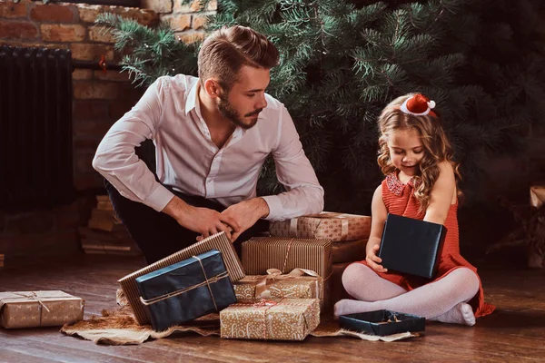 Pai e filha sentados em um chão cercado por presentes ao lado da árvore de Natal em casa . — Fotografia de Stock