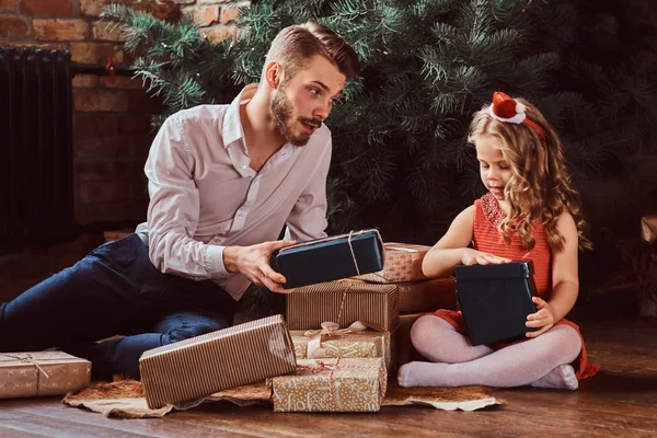 爸爸和女儿坐在家里圣诞树旁被礼物包围的地板上. — 图库照片