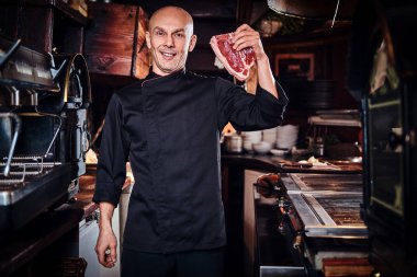 Şef giyen üniforma taze bir et parçası tutan ve bir kameraya bakarak gülen