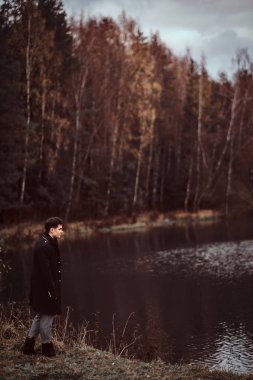 Yakışıklı bir genç adam yakın bir göl sonbahar ormandaki ayakta.