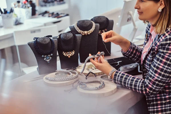 Mujer elegantemente vestida hace collares hechos a mano, trabajando con agujas e hilo en el taller . —  Fotos de Stock