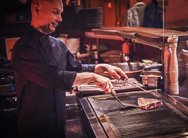 Zaměřil mistra kuchaře na sobě rovnoměrné vaření vynikající hovězí steak na kuchyni v restauraci. — Stock fotografie