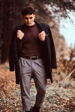 Omuzlarını sonbahar ormandaki kapsayan montlu genç adam.