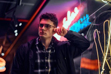 Dalgın bir genç adam sokakta bir ışıklı tabela üzerinde geceleri yaslanmış.