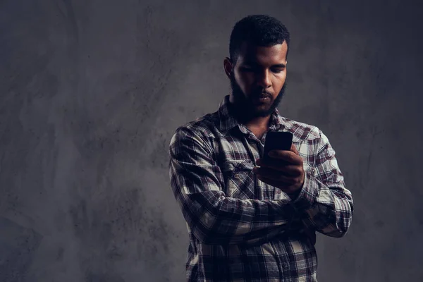Un afro-americano con la barba che indossa una camicia a scacchi con un telefono in uno studio . — Foto Stock