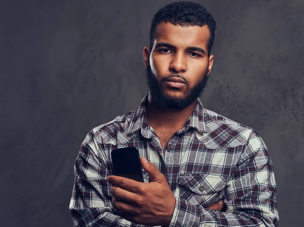 Afro-americano com barba a usar uma camisa de xadrez a segurar um telefone num estúdio . — Fotografia de Stock