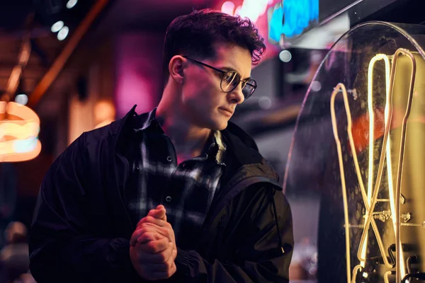 Een peinzende jonge man kijkend naar het verlichte uithangbord op straat 's nachts. — Stockfoto
