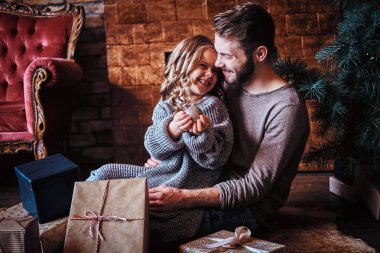 Sevimli küçük kız babasıyla bir yerde otururken Noel top tutan hediyeler tarafından çevrili mutluluk